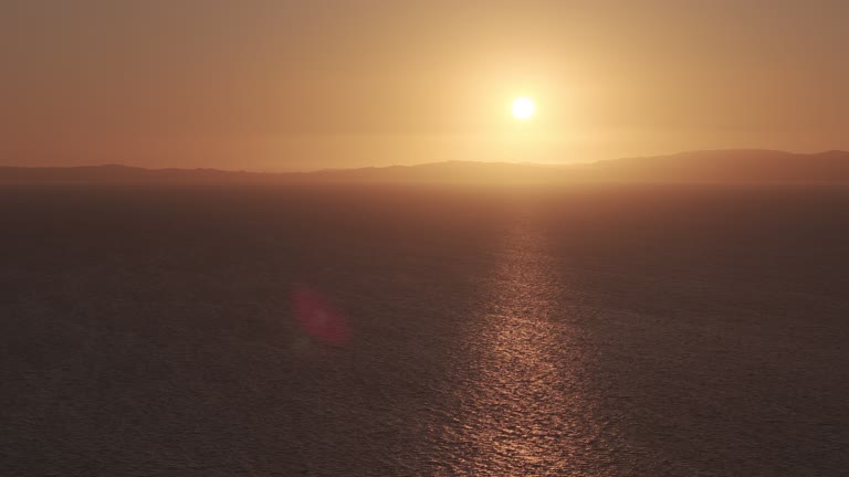 The low sun casts a golden reflection across the sea, with distant hills along the horizon.